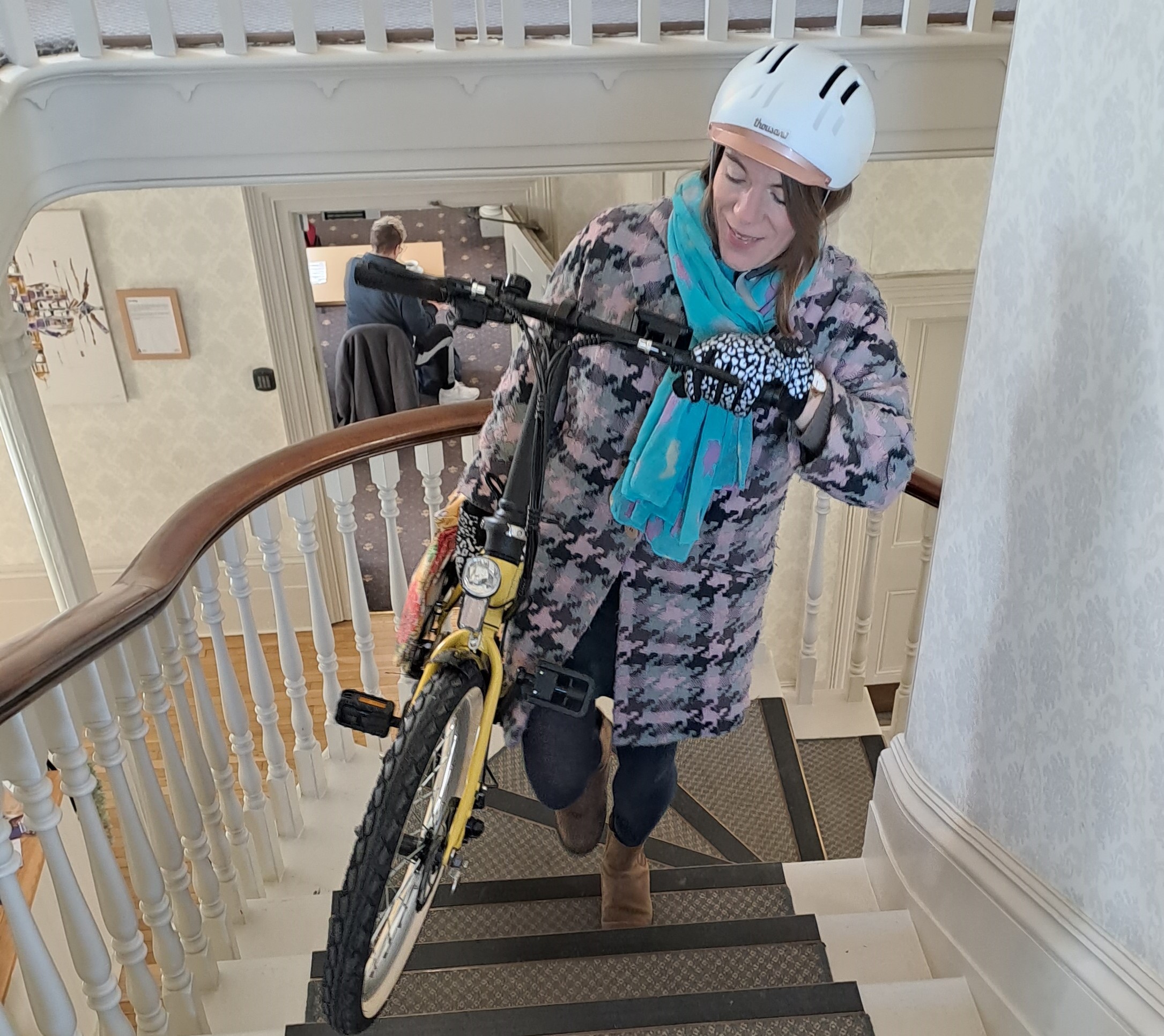 Caz Conneller walks up stairs with the Mycle compact folding electric bike in yellow